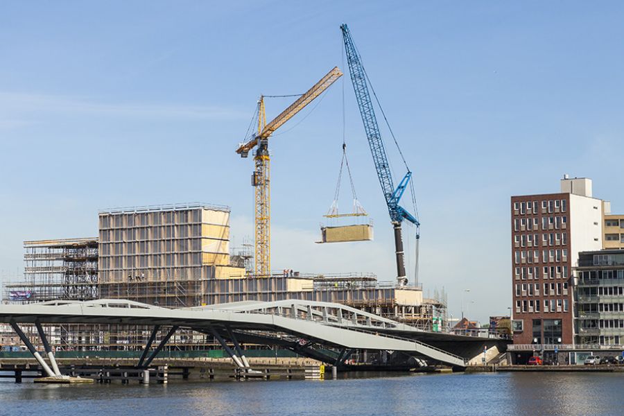 foto vanaf het water van een gebouw in aanbouw met twee kranen erboven en een brug ervoor
